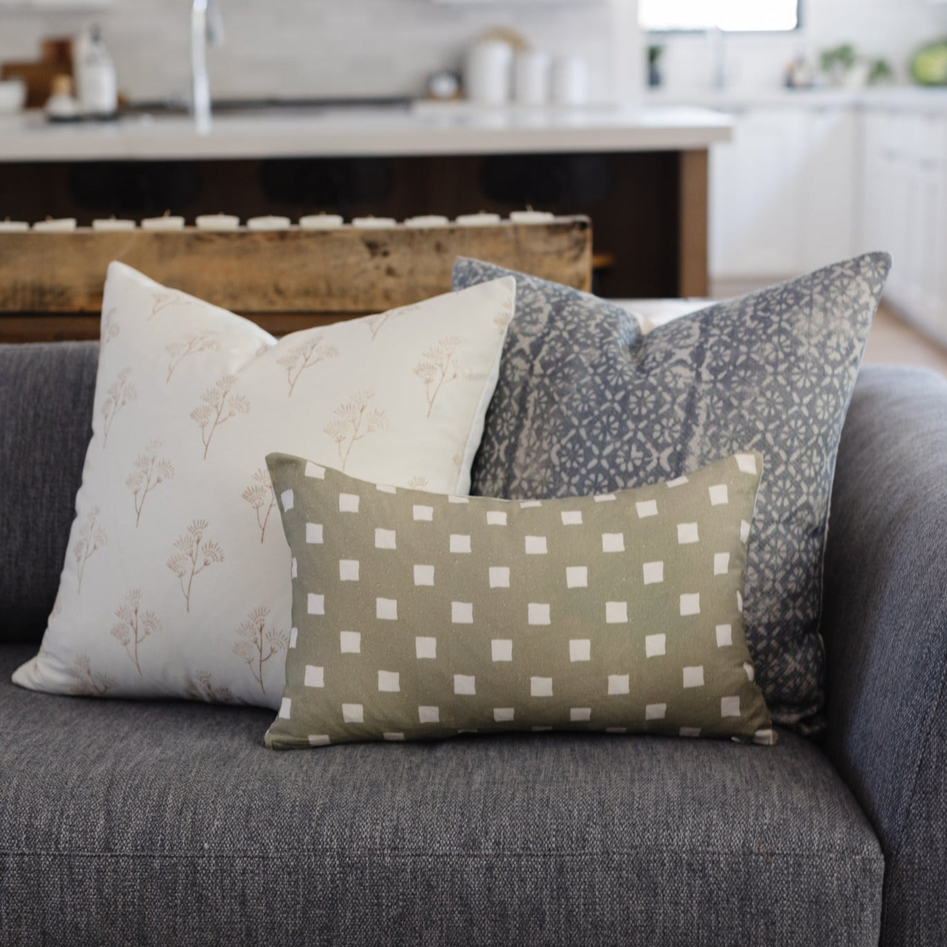 Olive green rectangular pillow with white diamond pattern displayed on gray sofa with coordinating pillows.