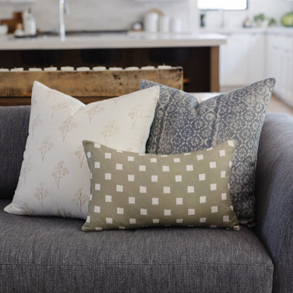 Olive green rectangular pillow with white diamond pattern displayed on gray sofa with coordinating pillows.
