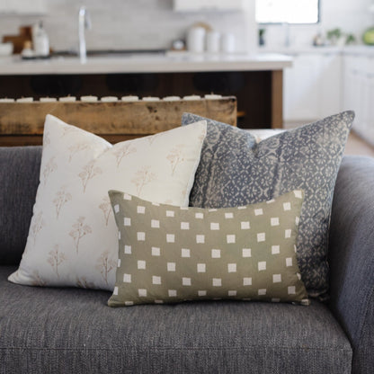 Three decorative pillows on a gray sofa: cream with thistle pattern, gray geometric diamond, and sage green with white dot gr