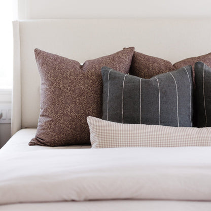 Tan and white gingham lumbar pillow displayed on a bed with coordinating brown and gray decorative pillows.