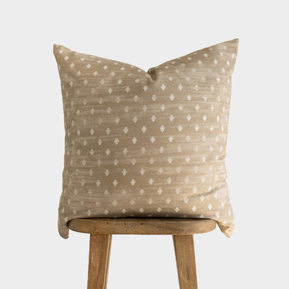 Beige pillow with white diamond pattern displayed on wooden stool.