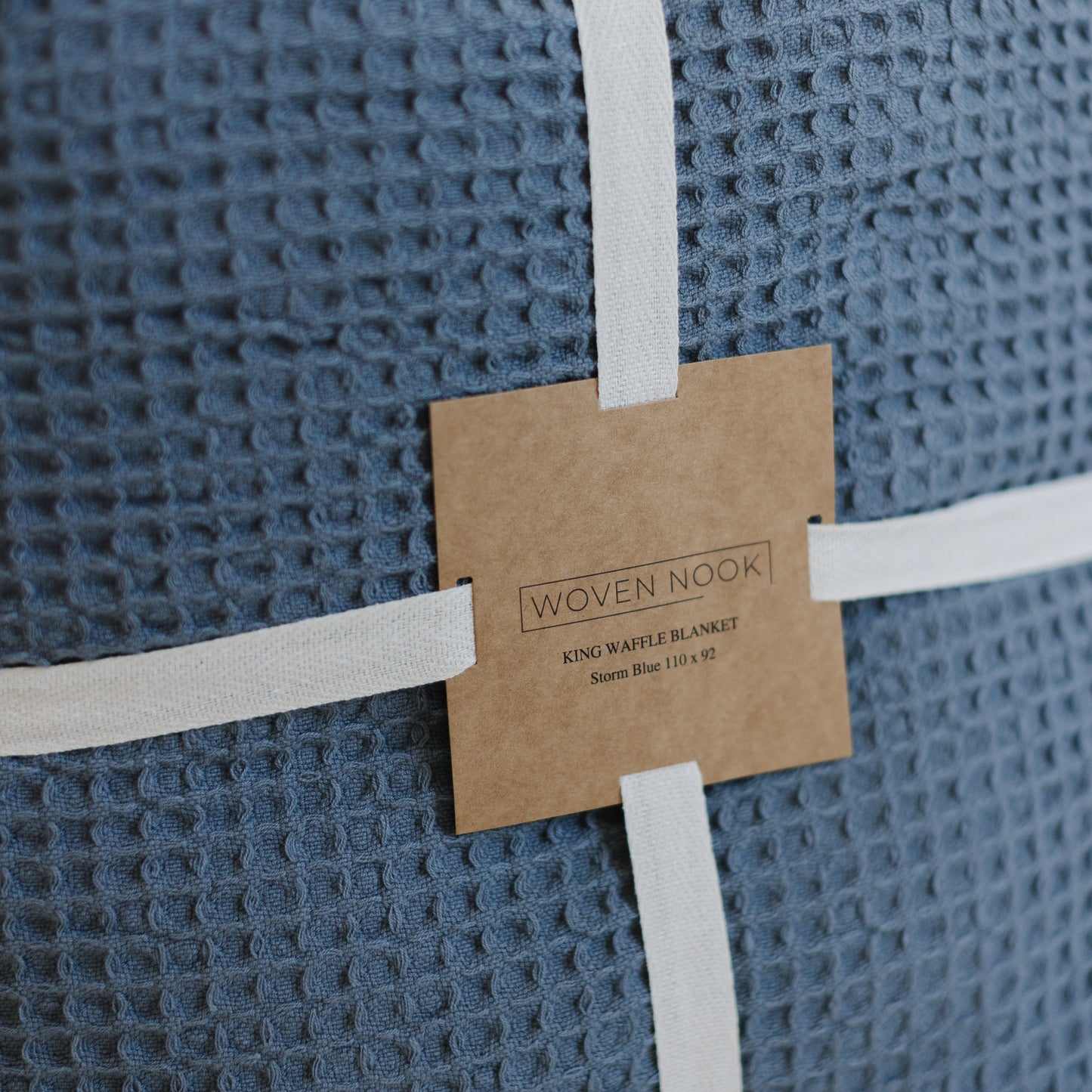 Storm blue waffle-textured blanket rolled and secured with white ribbon and kraft paper label from Woven Nook.