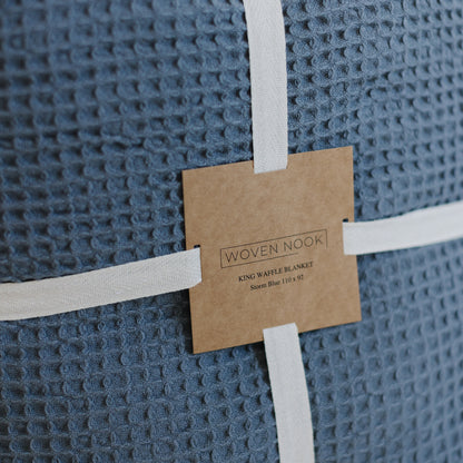 Storm blue waffle-textured blanket rolled and secured with white ribbon and kraft paper label from Woven Nook.