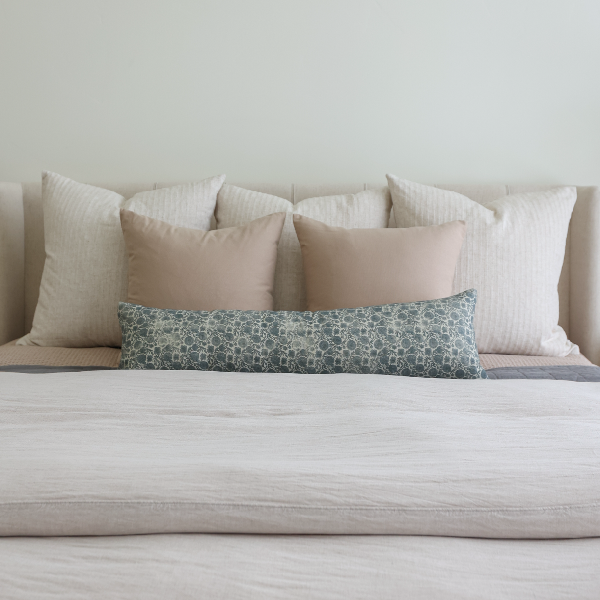 Tan and cream pillows in various sizes arranged on a bed with a teal patterned lumbar pillow.