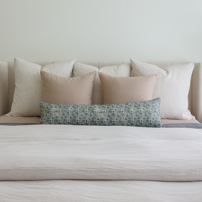 Tan and cream pillows in various sizes arranged on a bed with a teal patterned lumbar pillow.