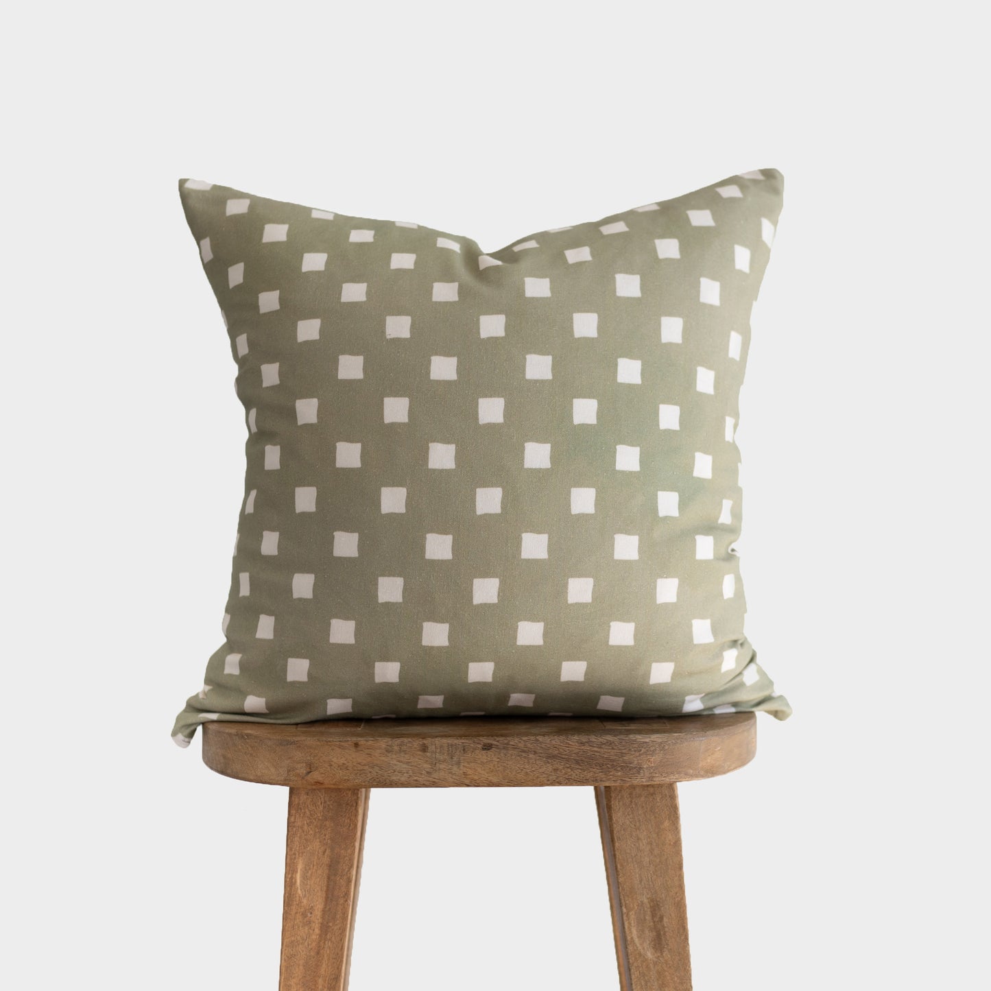 Olive green throw pillow with white spaced check pattern, displayed on a wooden stool.