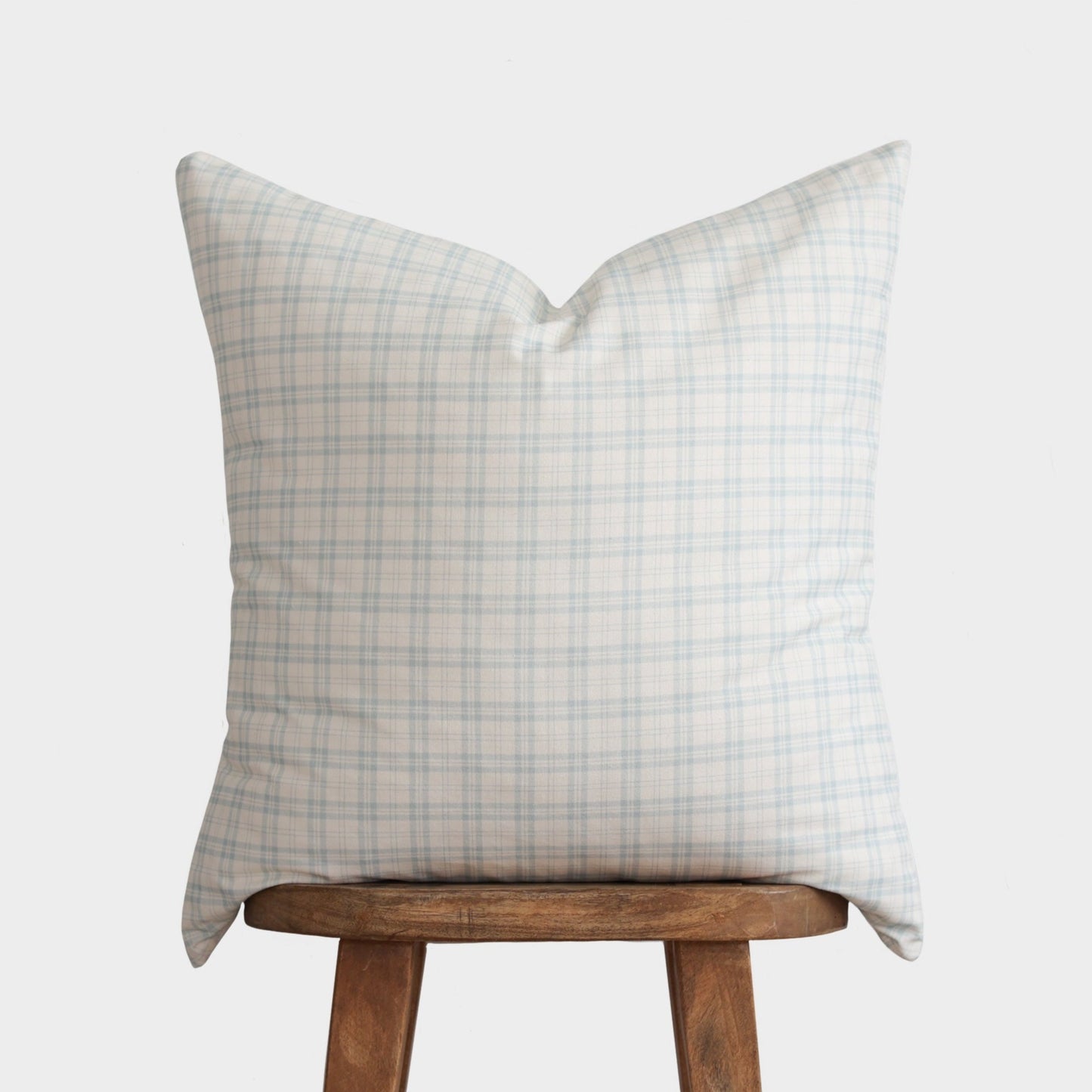 Light blue and beige plaid pillow with pointed corners displayed on a wooden stool.