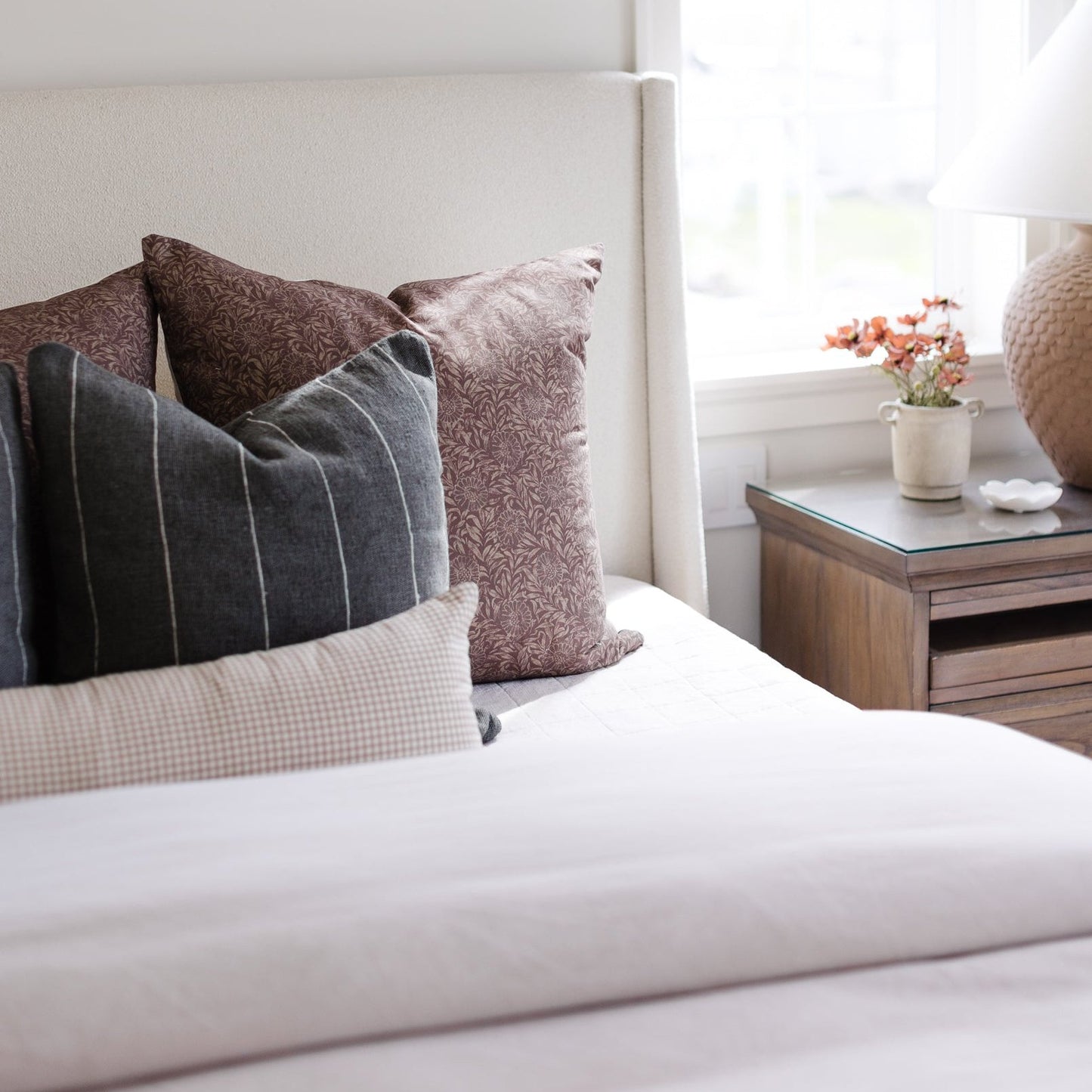 Tan and white gingham lumbar pillow displayed on a bed with other patterned pillows and bedding.