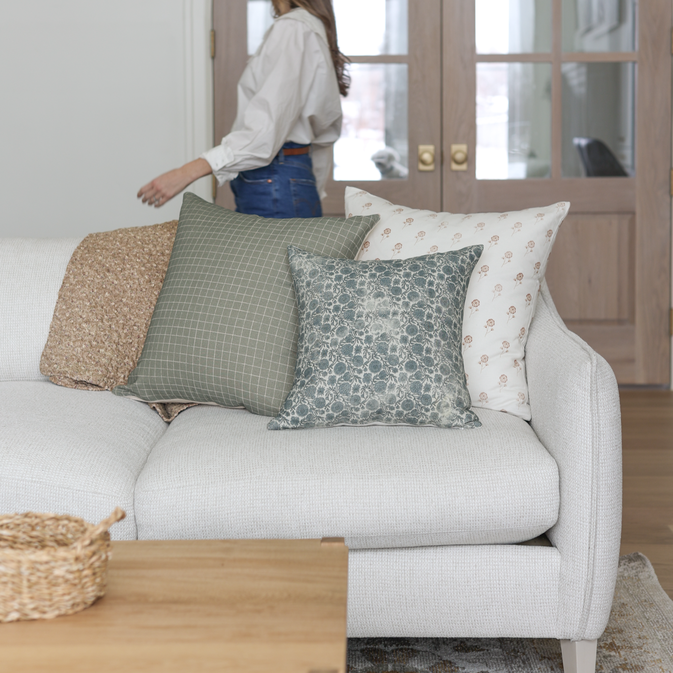 Four decorative pillows in green, cream, and patterned fabrics arranged on a white upholstered sofa.
