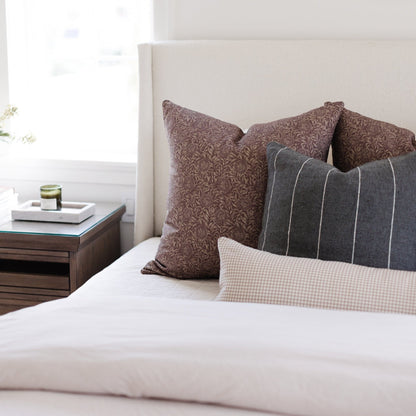 Tan and white mini gingham lumbar pillow displayed on a bed with coordinating pillows.