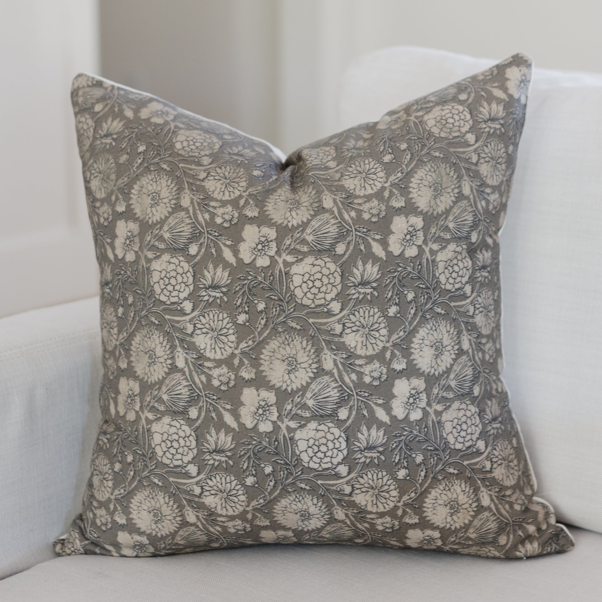 Gray and cream floral patterned square throw pillow with botanical motif on white upholstered furniture.