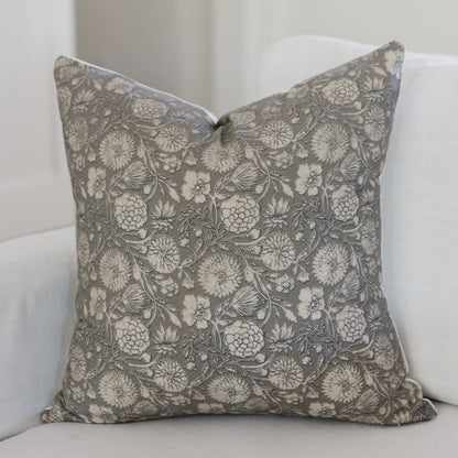 Gray and cream floral patterned square throw pillow with botanical motif on white upholstered furniture.