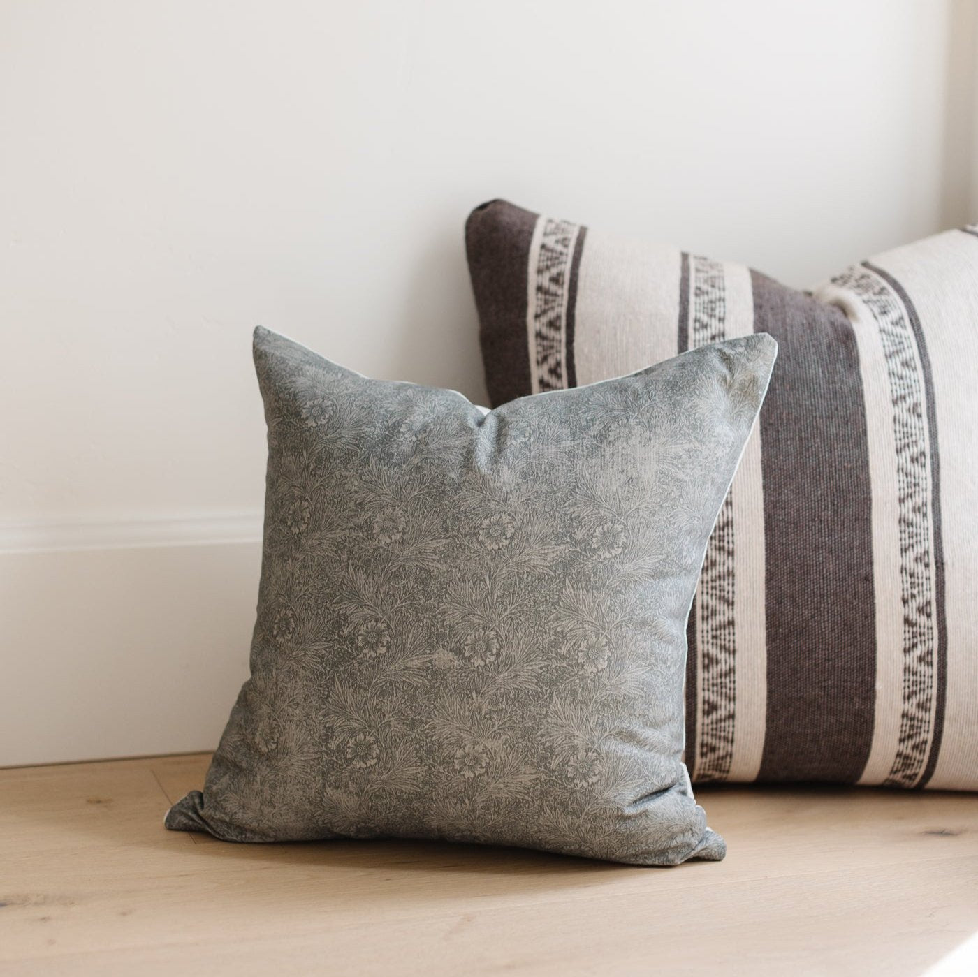 Gray damask patterned pillow displayed with striped cylindrical pillows on wooden floor.