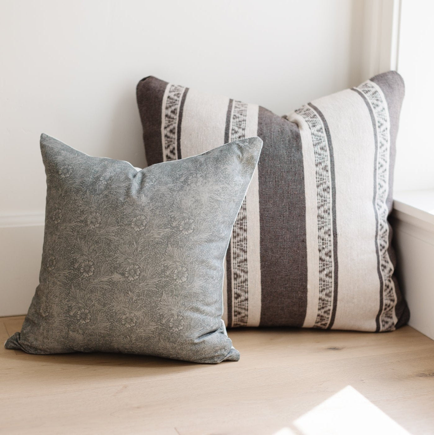 Two decorative pillows with gray damask and striped patterns with woven trim details.