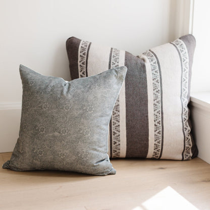 Two decorative pillows with gray damask and striped patterns with woven trim details.