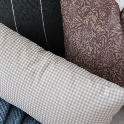 Tan and white gingham lumbar pillow displayed with other patterned pillows on furniture.