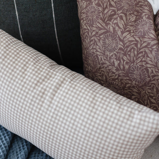 Tan and white gingham lumbar pillow displayed with other patterned pillows on furniture.
