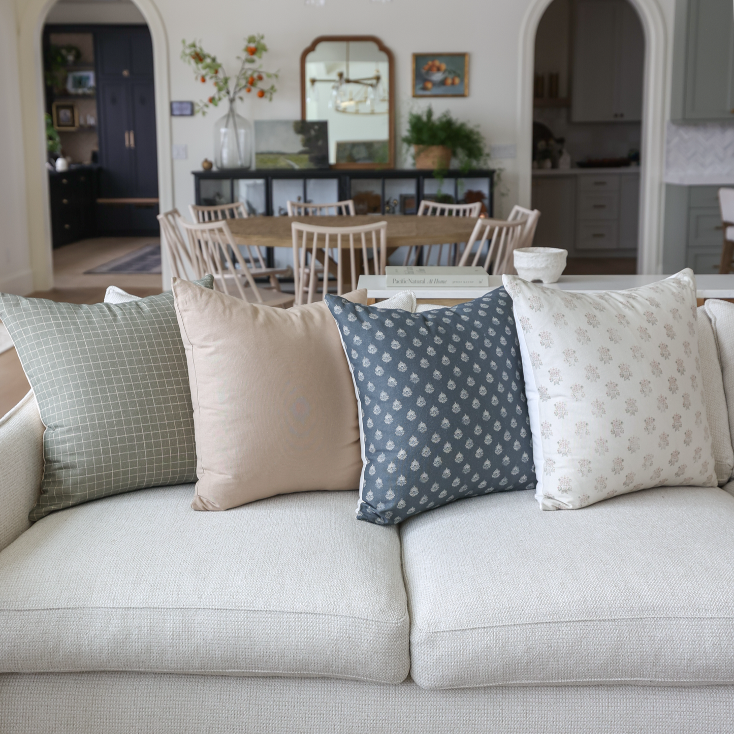 Four tan and blue patterned throw pillows arranged on a beige sofa in a living room setting.