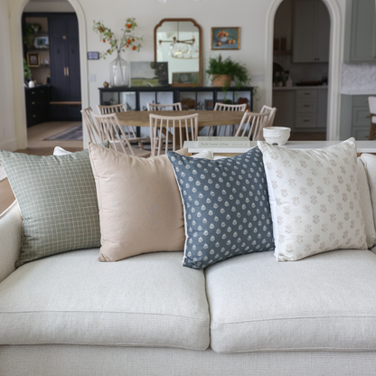 Four tan and blue patterned throw pillows arranged on a beige sofa in a living room setting.