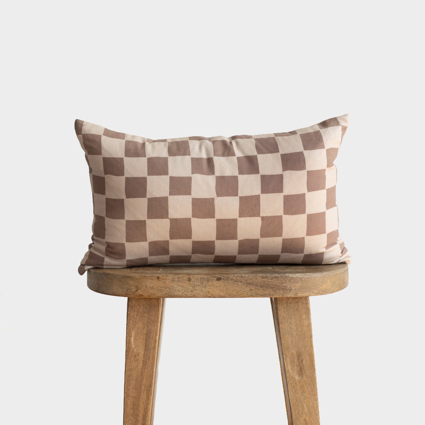 Tan and brown checkered pillow displayed on a wooden stool against a neutral background.
