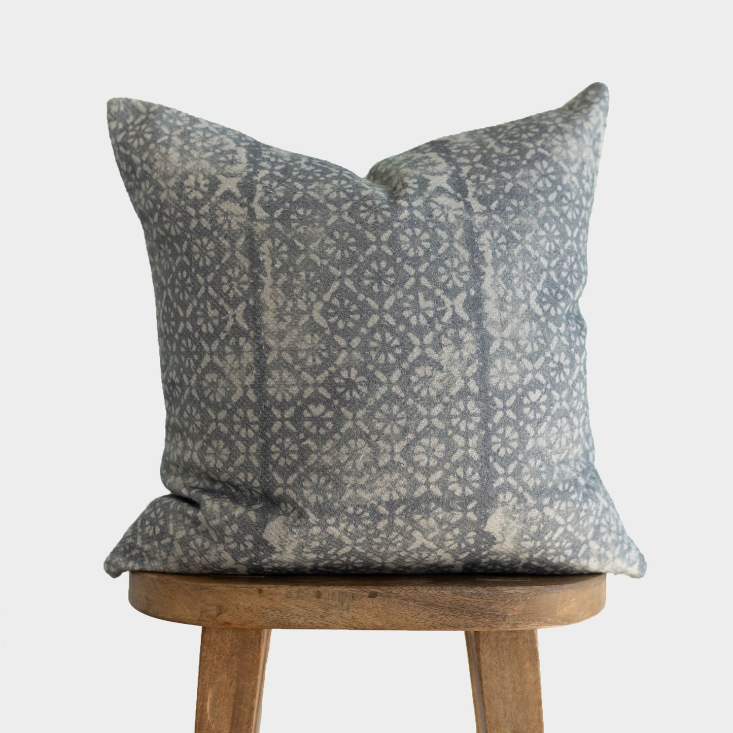 Gray and cream diamond floral patterned pillow with thick weave fabric displayed on wooden stool.