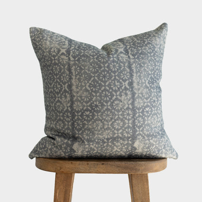 Gray and cream diamond floral patterned pillow with thick weave fabric displayed on wooden stool.