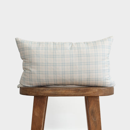 Cream and blue plaid lumbar pillow on wooden stool against white background.