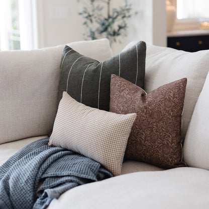 Tan and white small gingham check lumbar pillow displayed on a light sofa with other pillows.