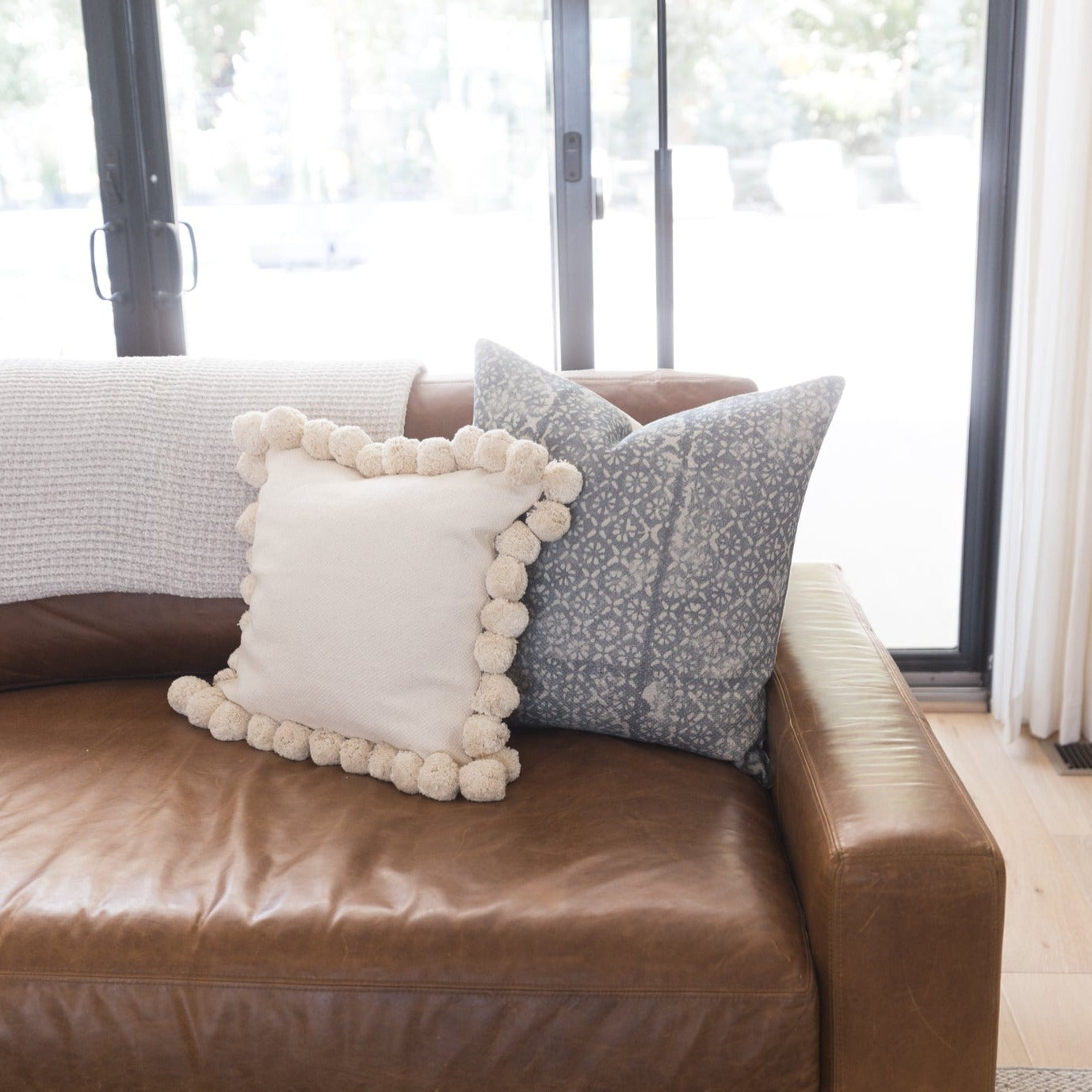 Gray diamond floral patterned throw pillow with thick weave displayed on brown leather sofa.