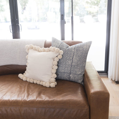 Gray diamond floral patterned throw pillow with thick weave displayed on brown leather sofa.