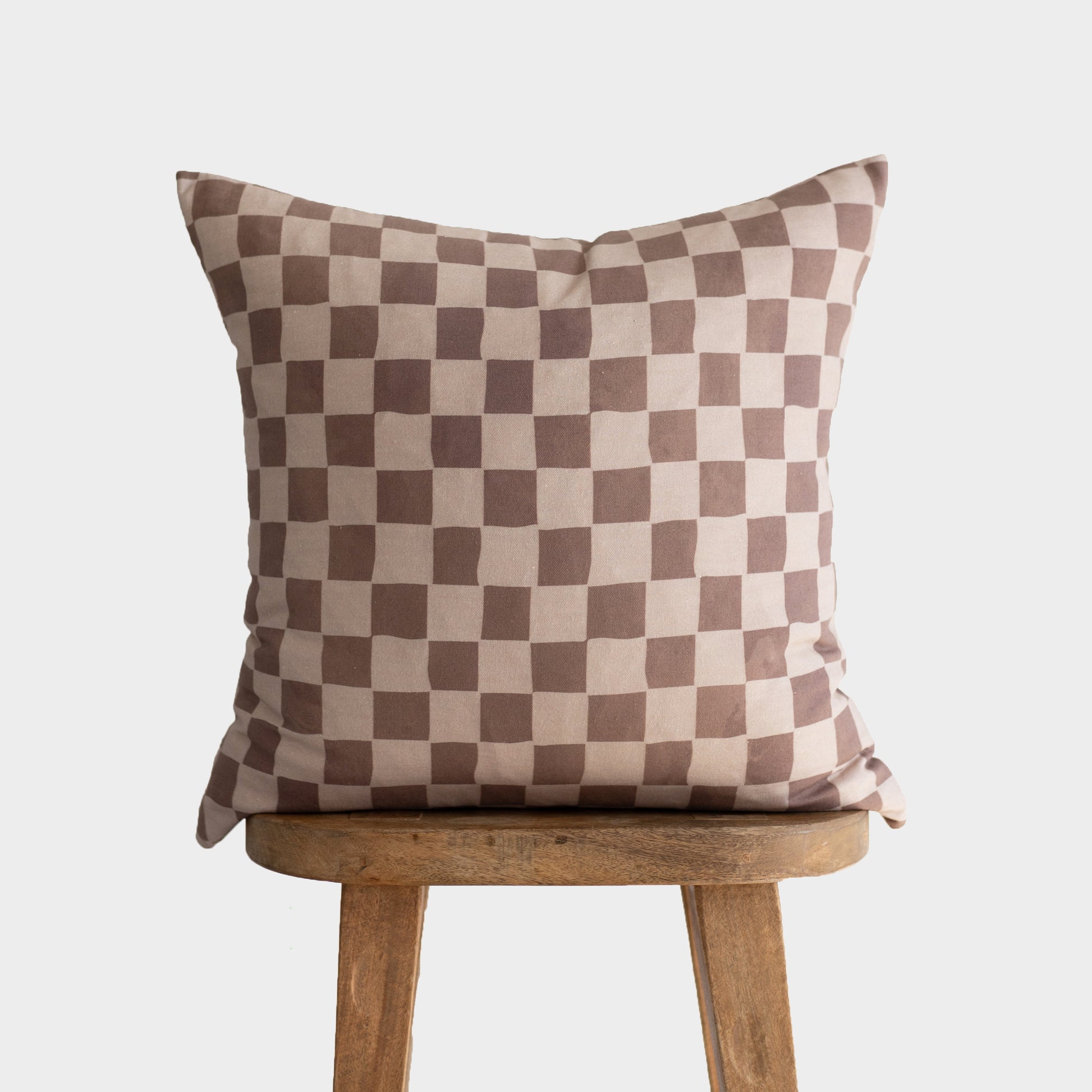 Tan and brown checkered pillow with alternating square pattern displayed on wooden stool.