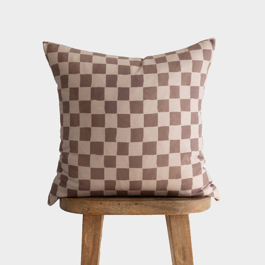 Tan and brown checkered pillow with alternating square pattern displayed on wooden stool.