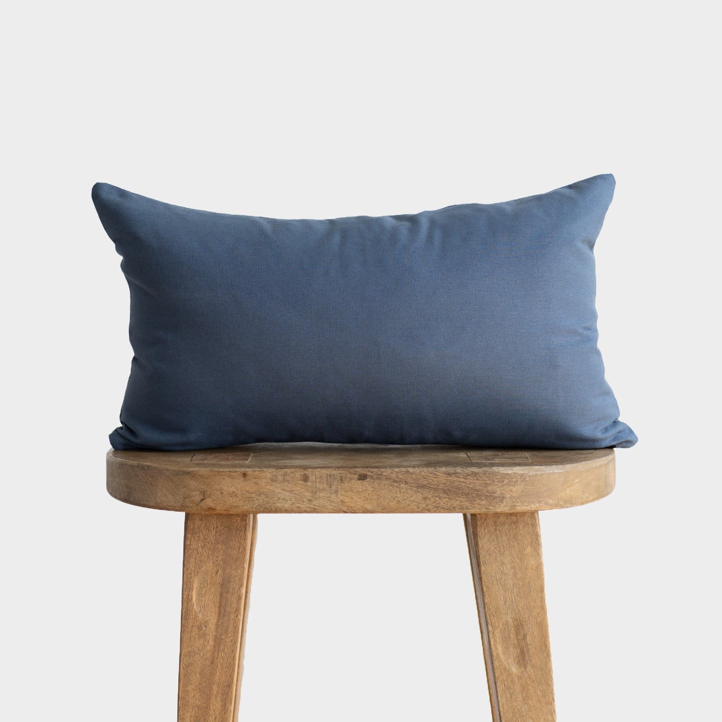 Navy blue rectangular pillow with solid fabric displayed on wooden stool.