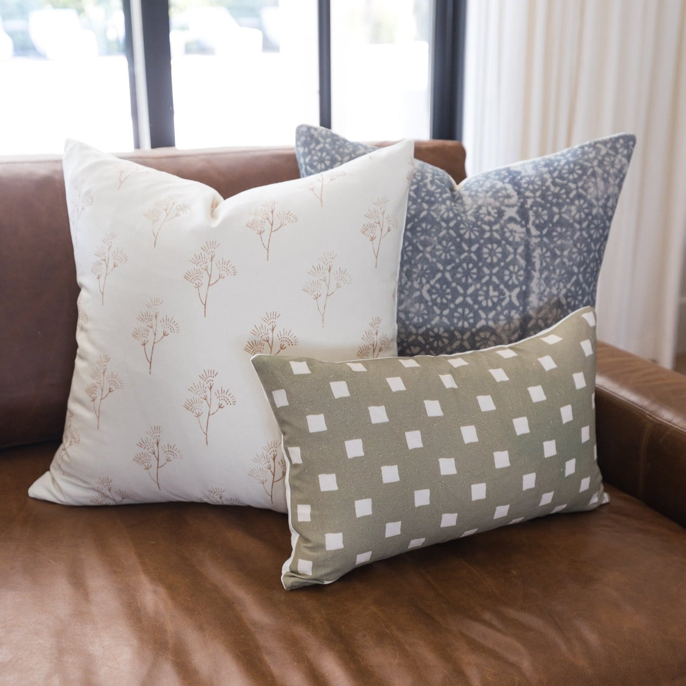 Olive and white spaced check pillow displayed on brown leather sofa with coordinating pillows.