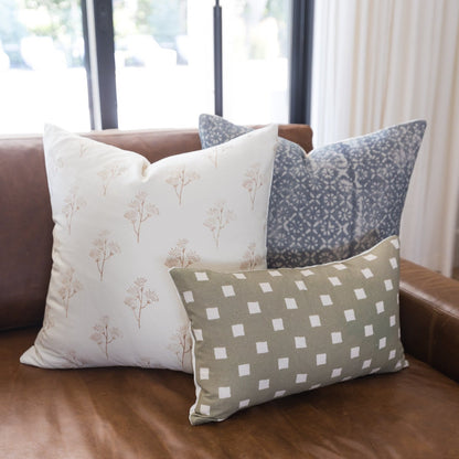 Three decorative pillows with floral and geometric patterns in cream, gray, and taupe on a brown leather sofa.