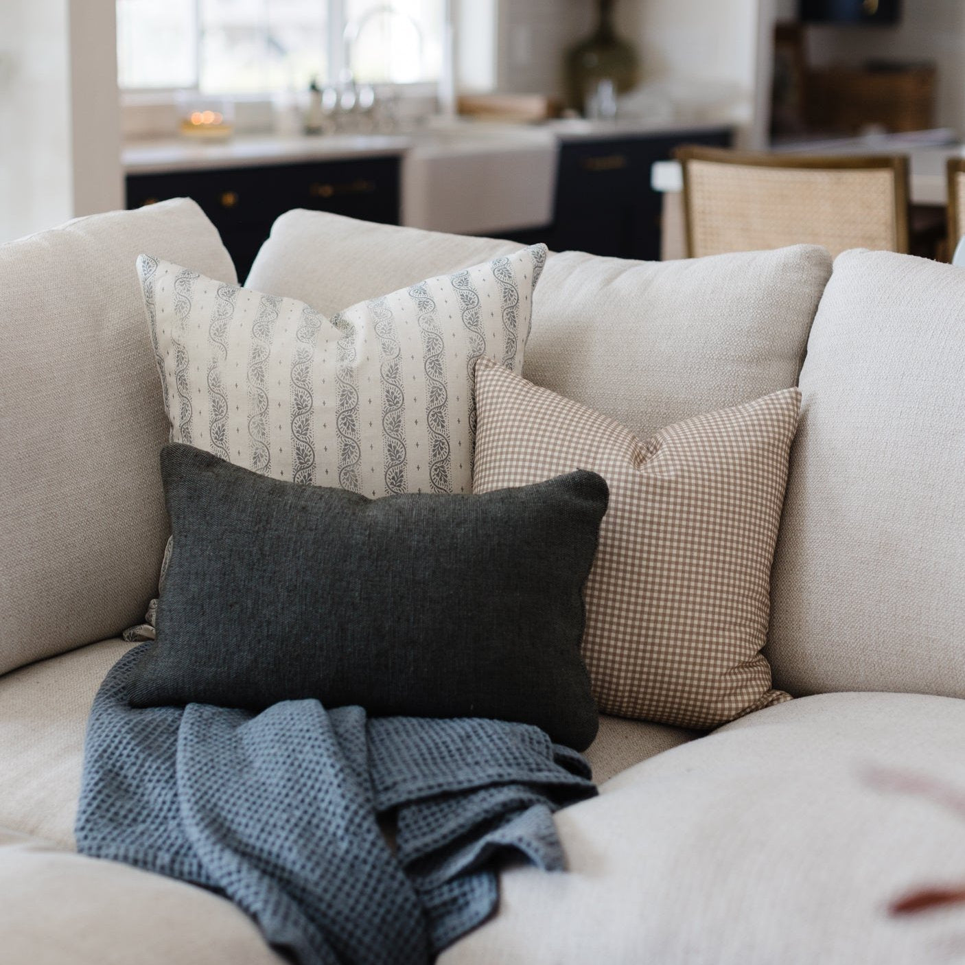 Decorative pillows with paisley, gingham, and solid patterns displayed on a cream-colored sofa.