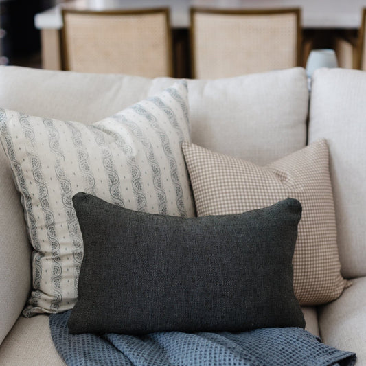 Tan gingham patterned pillow displayed among other decorative pillows on a beige sofa.