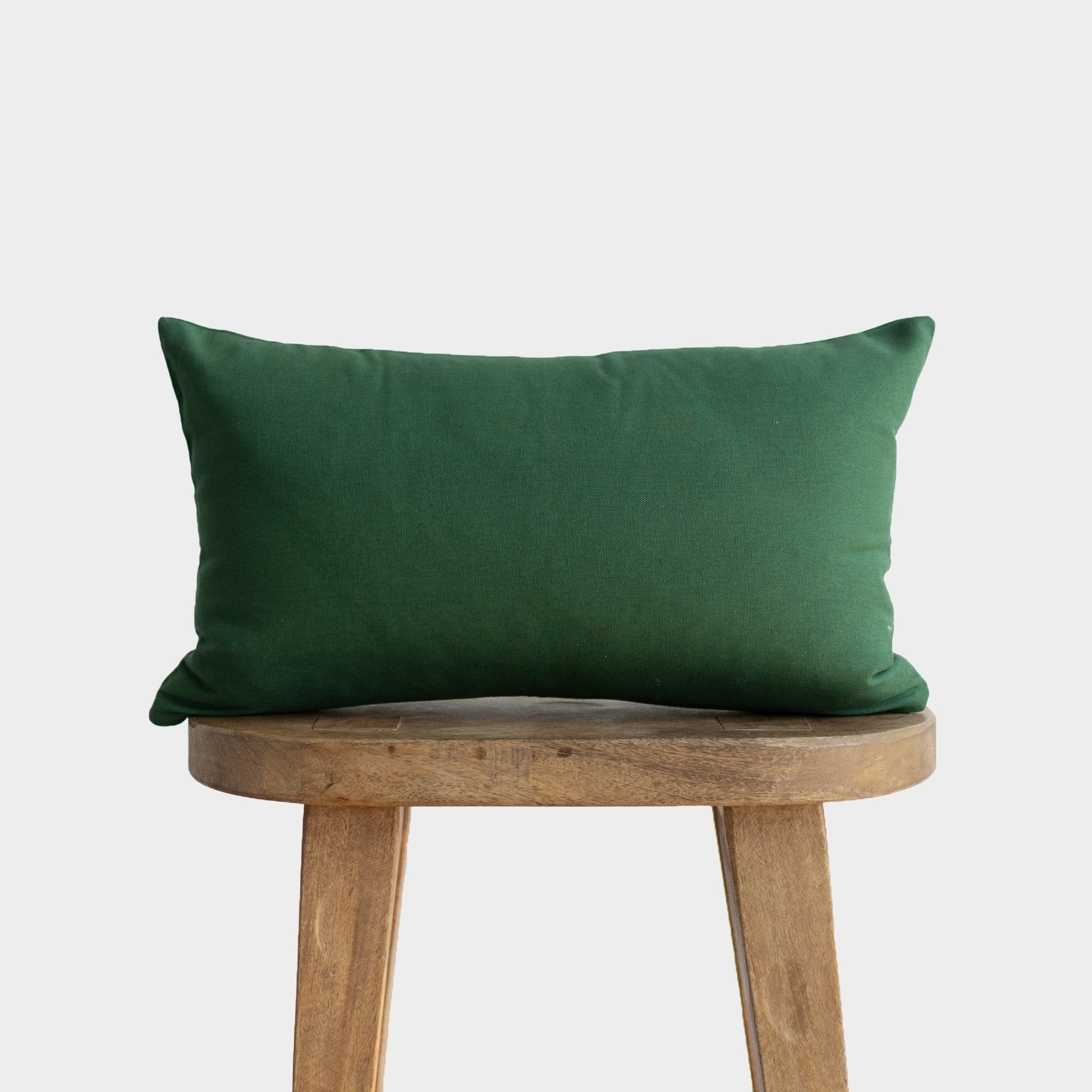 Dark green rectangular pillow with linen texture placed on a wooden stool.