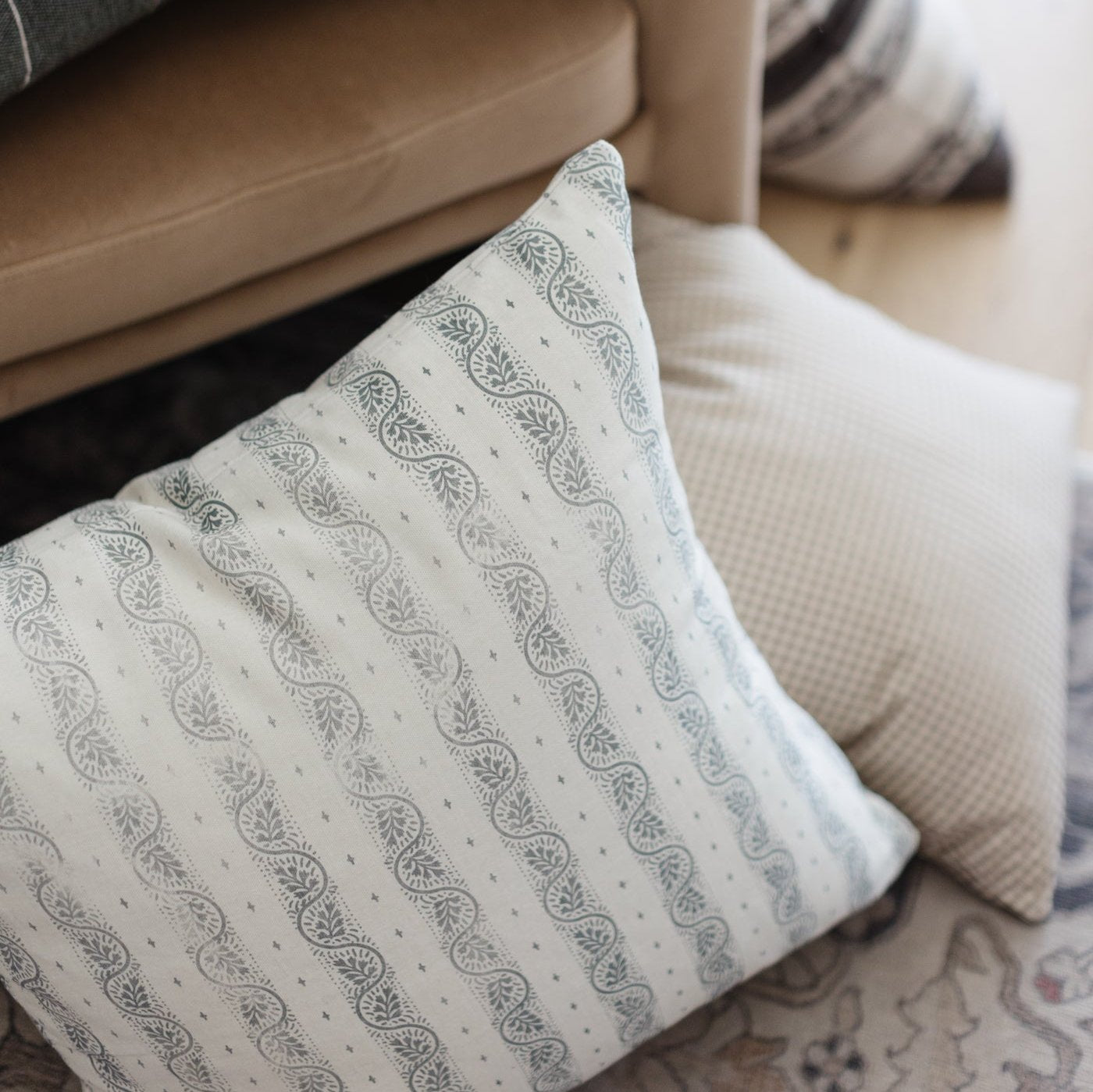 Cream throw pillow with gray leaf and dot stripe pattern, displayed on beige sofa.