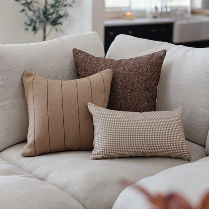 Tan and white gingham lumbar pillow displayed on a beige sofa with coordinating pillows.