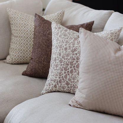 Four throw pillows in neutral tones with geometric, floral, and gingham patterns arranged on a light-colored sofa.