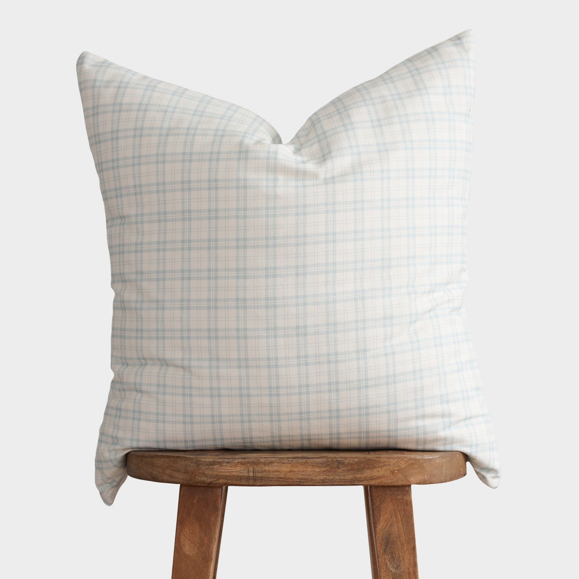 Light blue and cream plaid pillow cover displayed on a wooden stool.