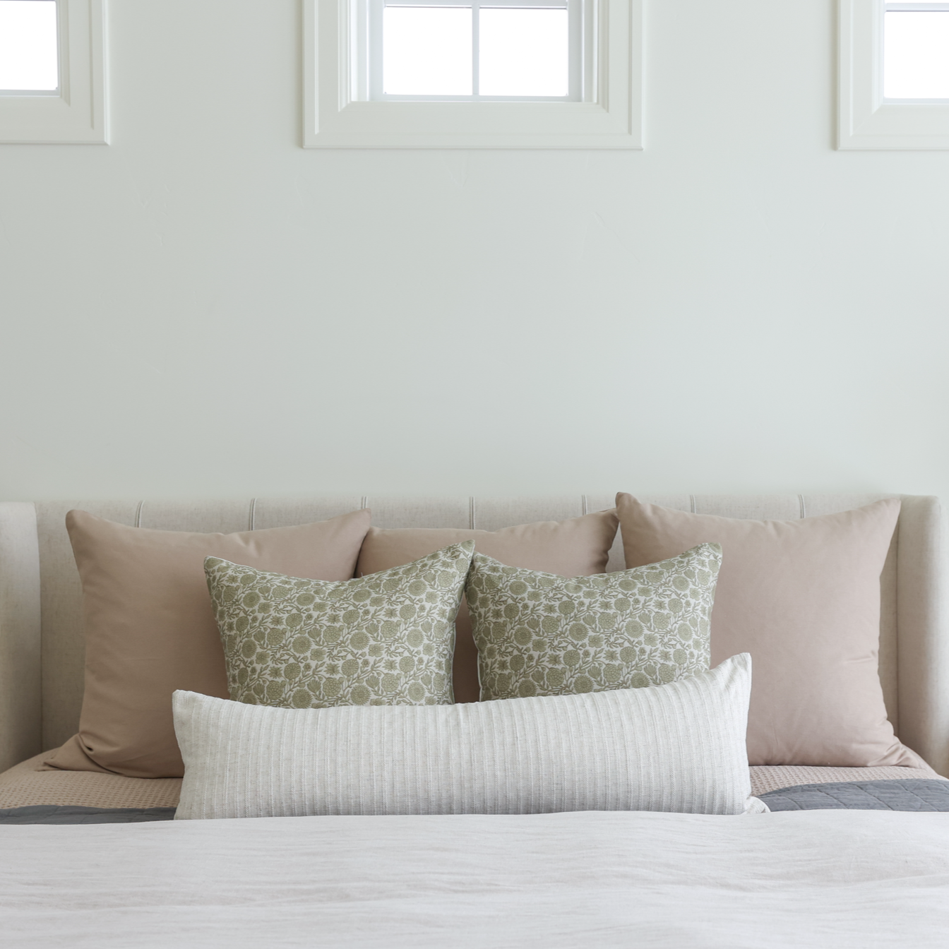 Green floral patterned pillow displayed on a bed with neutral-toned pillows and white striped lumbar pillow.