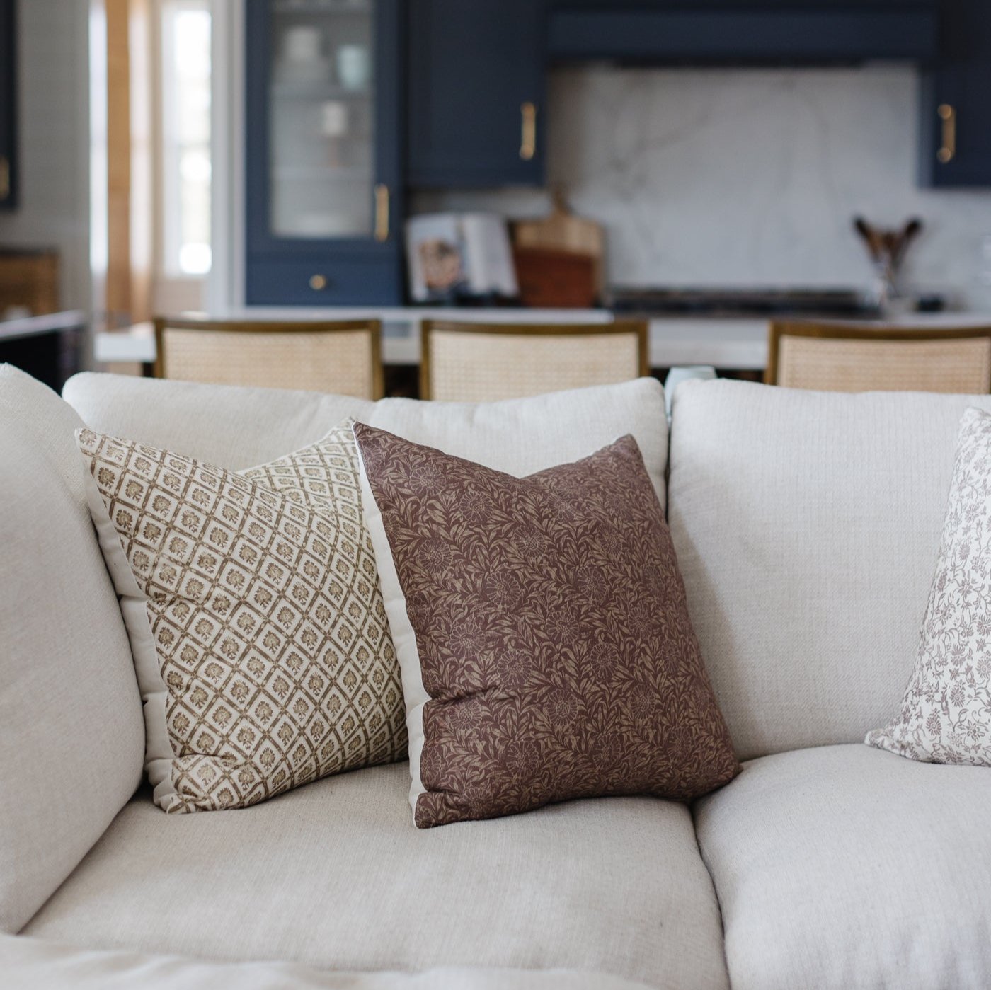 Four decorative pillows in neutral tones with geometric and floral patterns arranged on a cream sofa.