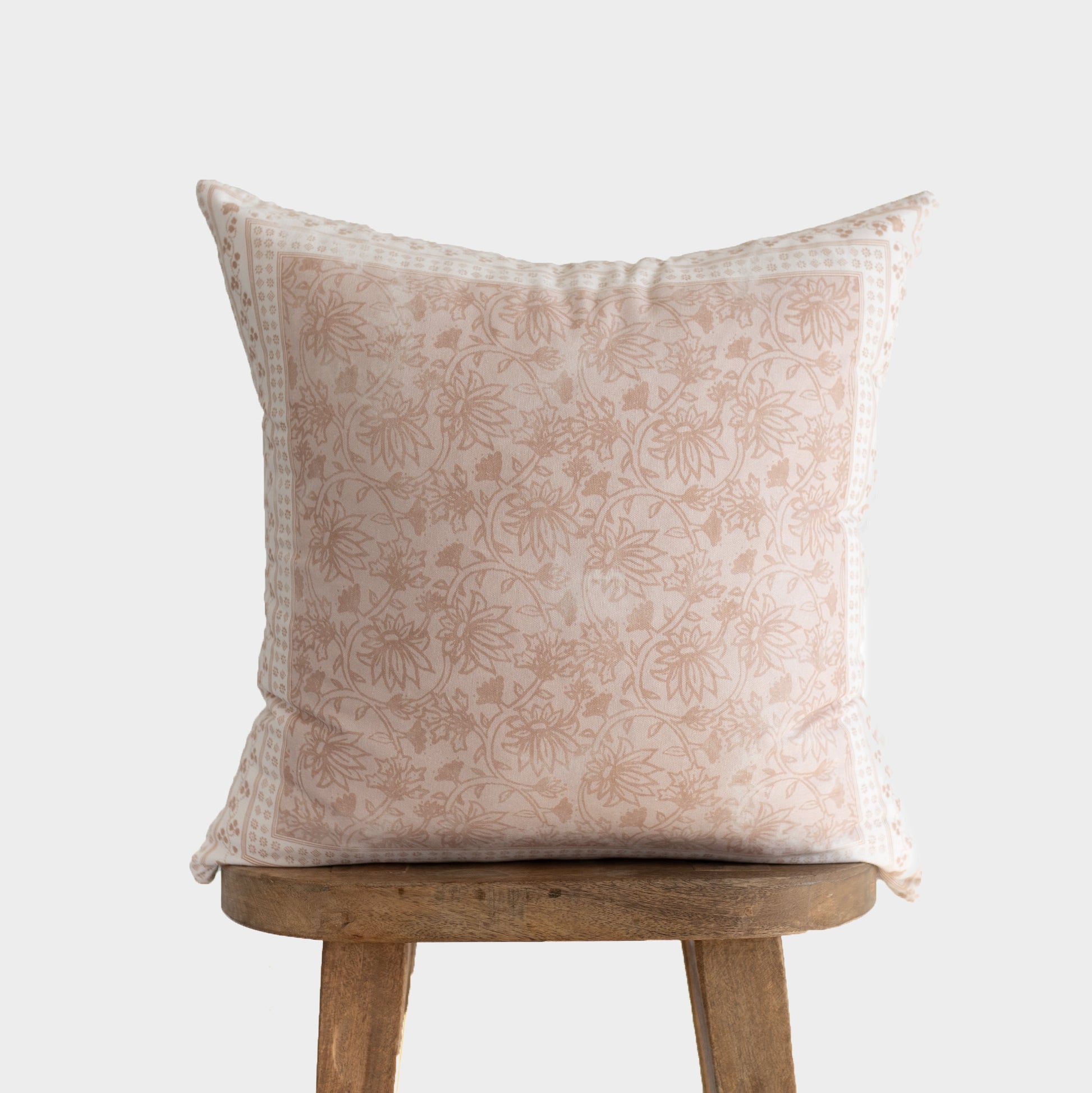 Cream and tan floral patterned throw pillow displayed on a wooden stool.