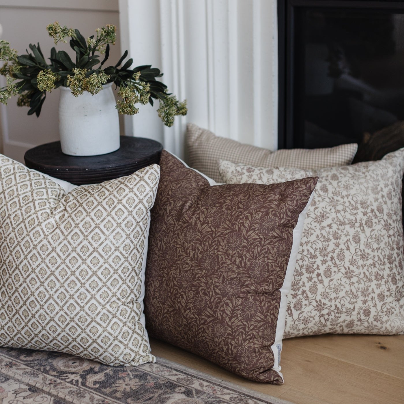 Four throw pillows in neutral tones with geometric and floral patterns, displayed on a sofa with a potted plant arrangement.