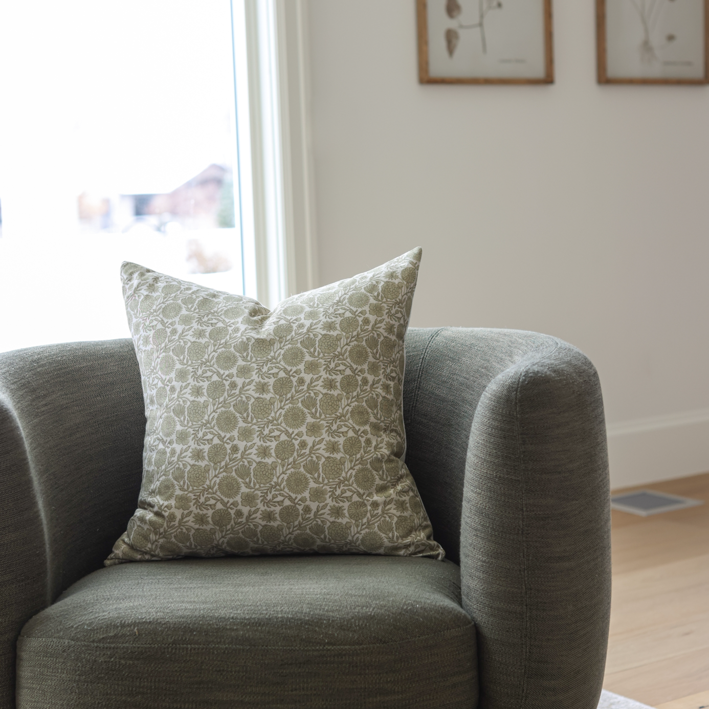 Green and cream patterned square pillow displayed on a gray upholstered armchair.