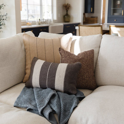 Rectangular lumbar pillow with alternating dark gray and cream horizontal stripes on a beige sofa.