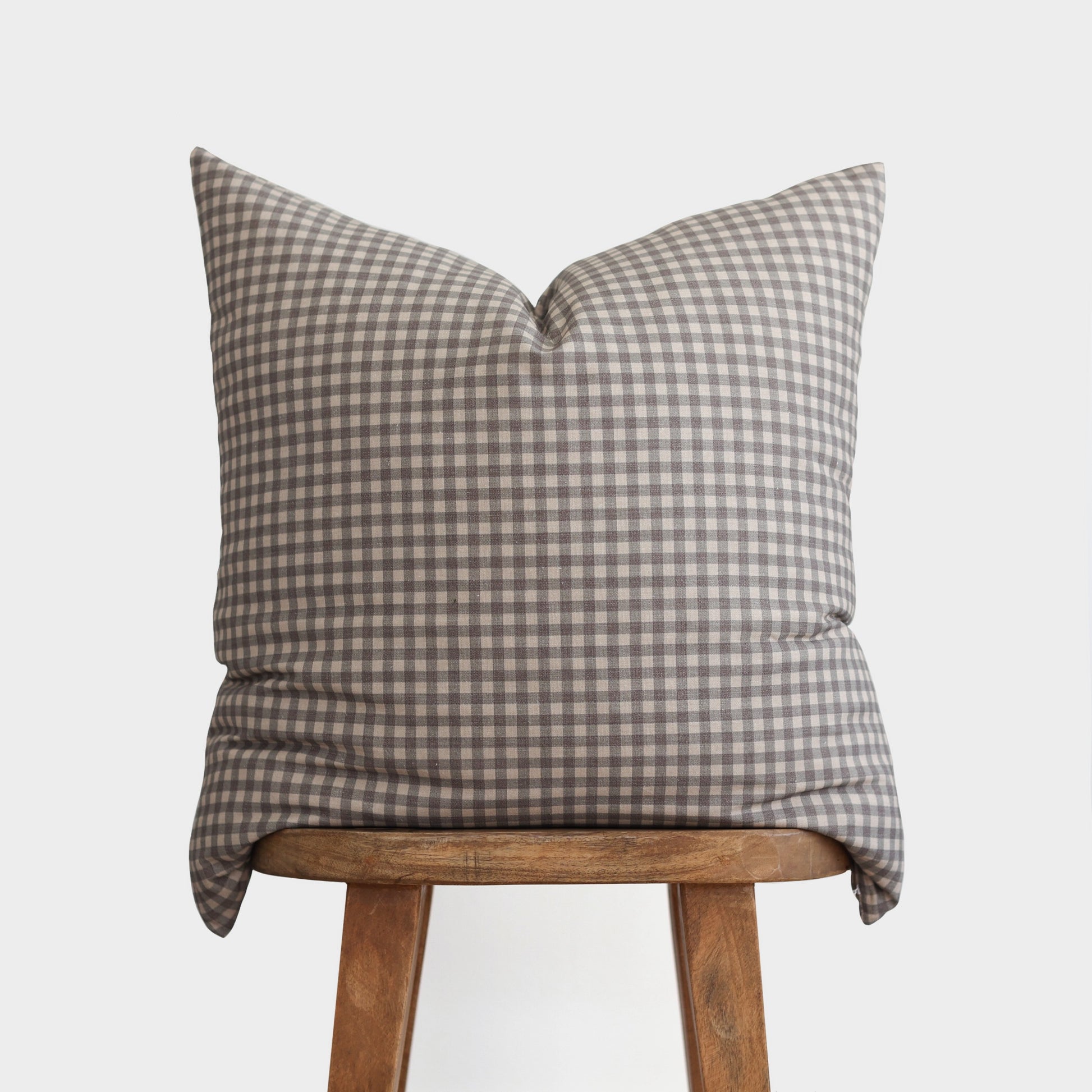 Brown and white gingham patterned pillow cover displayed on a wooden stool.