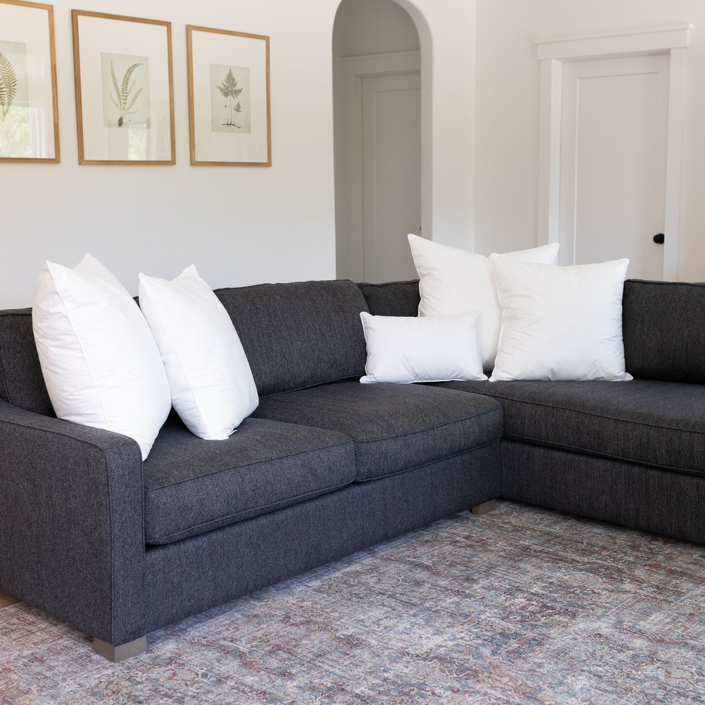Five white rectangular throw pillows arranged on a dark gray sectional sofa.